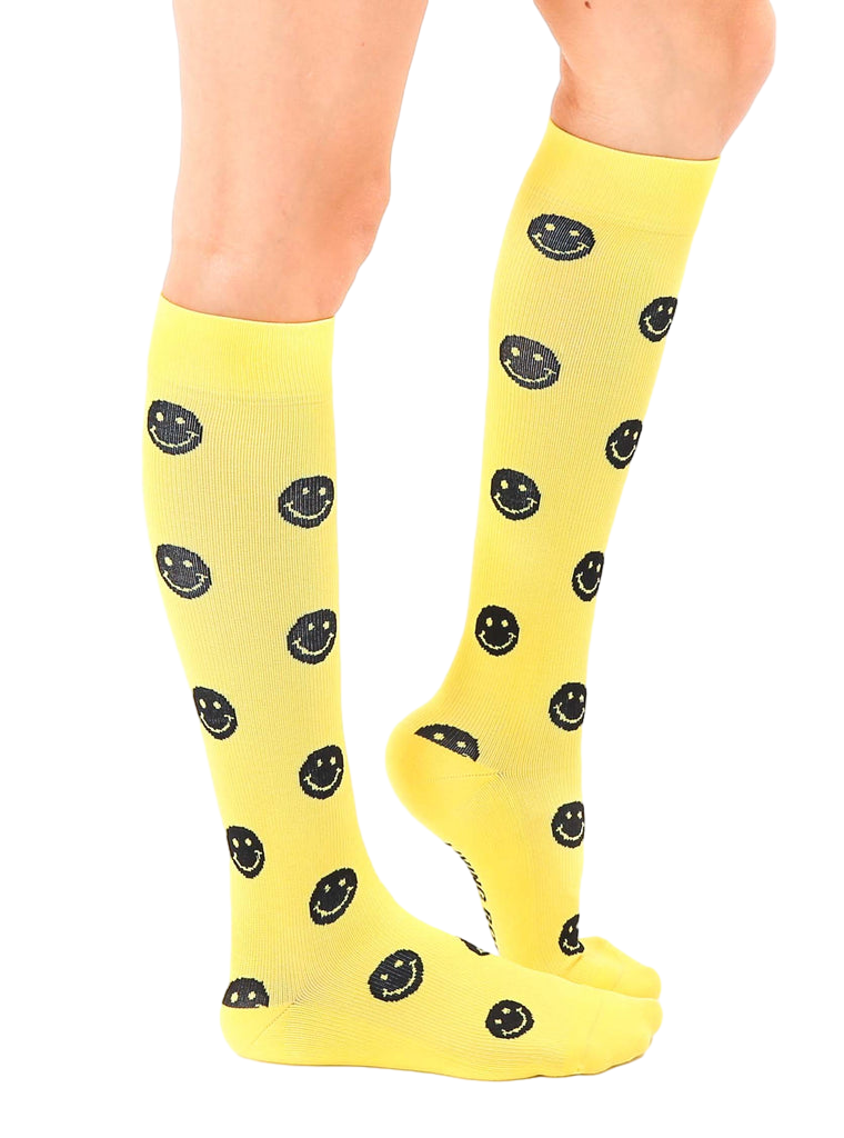 Lifestyle shot showing yellow smiley face knee-high socks on a model's legs. [lf]