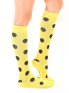 A pair of yellow knee-high socks with a pattern of black smiley faces. The socks have the words 