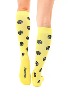 A pair of yellow knee-high socks with a pattern of black smiley faces. The socks have the words 