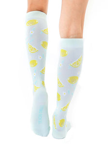 A pair of light blue knee-high socks with a pattern of lemons and white flowers.