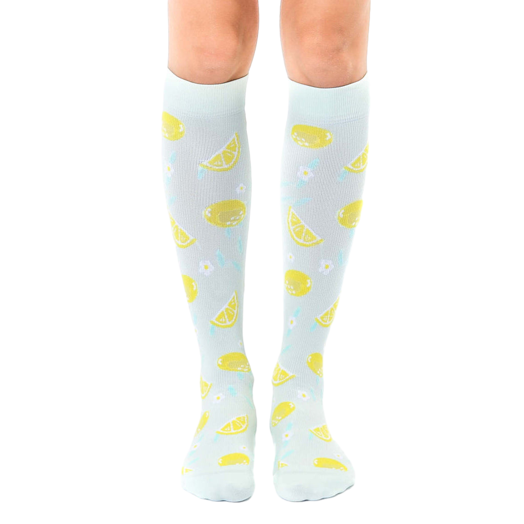 Pair of light blue knee-high socks with a lemon and flower pattern.  The lemons are yellow and the flowers are light teal. [lf]