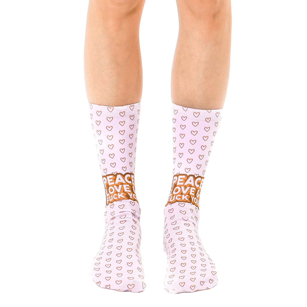 A pair of women's crew socks in light pink.  Tiny hearts cover the socks, with a 'Peace Love Fuck You' message near the ankle in a light brown color. [lf]