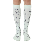 Pair of mint green knee-high socks with a pattern of stethoscopes, heartbeats, and syringes. [lf]