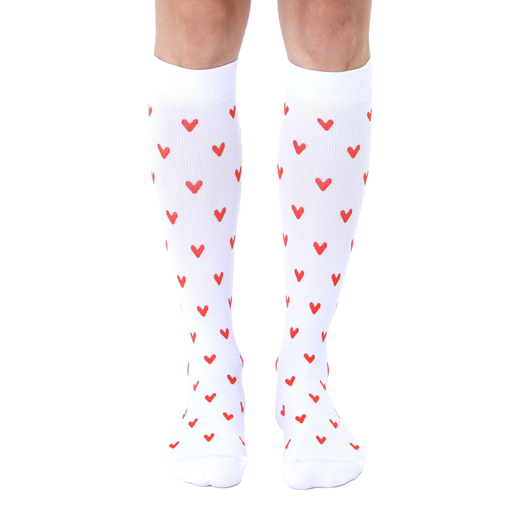 Pair of white knee-high socks with a repeating pattern of small red hearts. [lf]