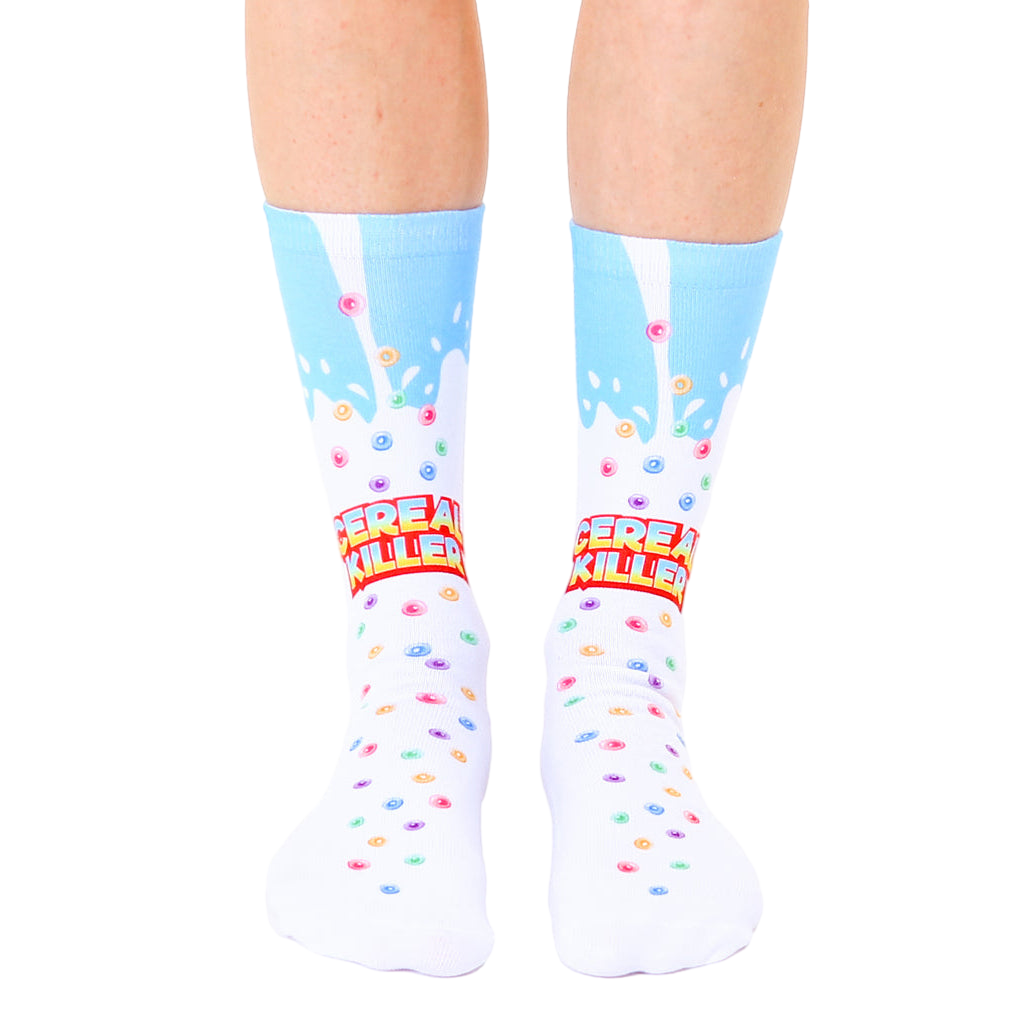 A pair of white crew socks with a light blue milk splash design and colorful cereal pieces. The text 'Cereal Killer' is prominently displayed. [lf]