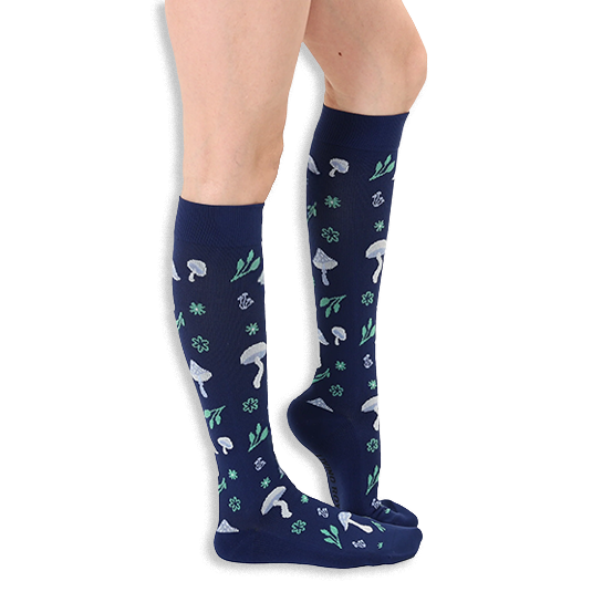 Side profile of a person wearing navy blue knee-high socks patterned with light blue mushrooms and mint green foliage.