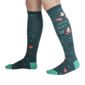 Lifestyle shot showing the 'Drop It Like It's Hot' socks on a person's legs.  The teal and green colors pop against the dark background.
