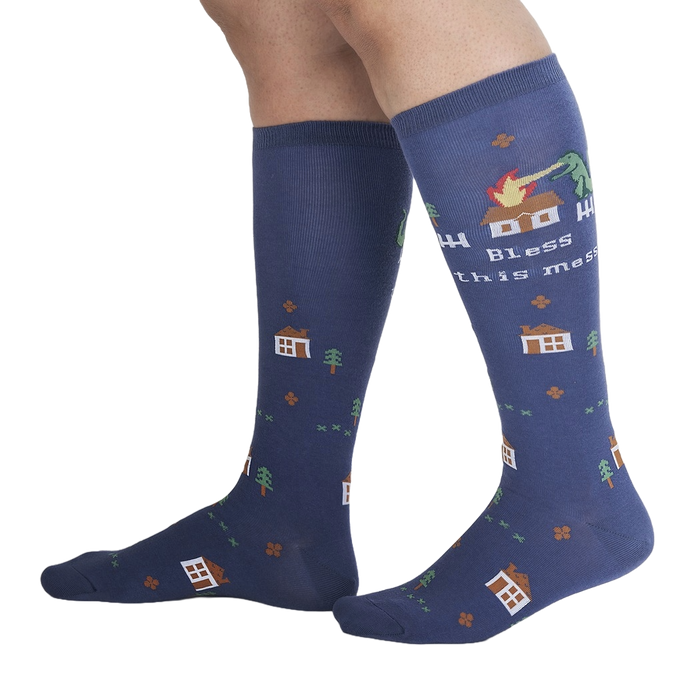 A pair of blue socks with a pixelated dinosaur on them. The dinosaur is breathing fire on a house. The socks have the words 