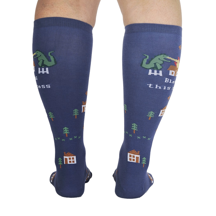 A pair of blue socks with a pixelated dinosaur on them. The dinosaur is breathing fire on a house. The socks have the words 