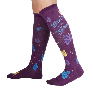 A pair of purple knee-high socks with a repeating pattern of blue and gold crystals and the words 