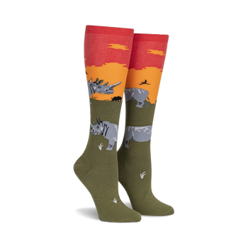 green socks with orange top and ribbed detail, featuring gray rhinos, black birds and orange plants on green field with sunset. knee high. women.   