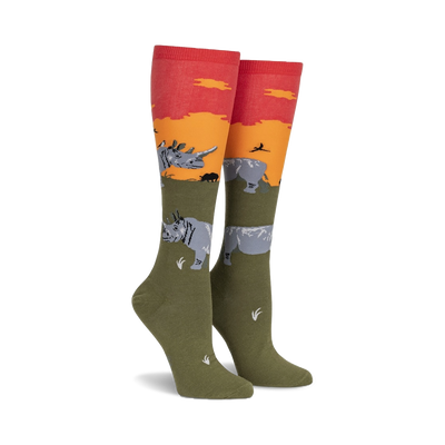 green socks with orange top and ribbed detail, featuring gray rhinos, black birds and orange plants on green field with sunset. knee high. women.   