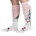 Lifestyle shot of model wearing pink and white knee-high socks with a winter scene.