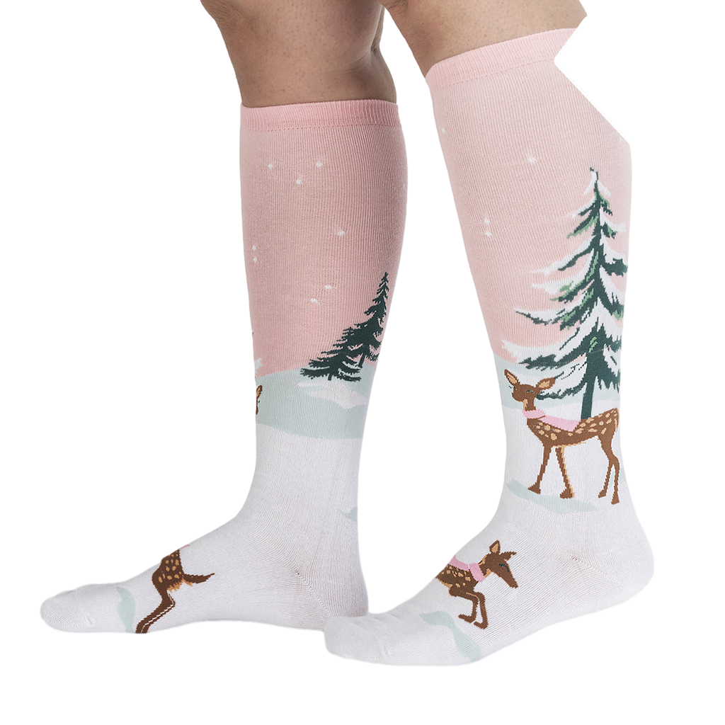 Lifestyle shot of model wearing pink and white knee-high socks with a winter scene.