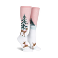 Pair of women's knee-high socks. Pink and white with a winter scene: deer wearing scarves, snowy trees. 