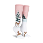 Pair of women's knee-high socks. Pink and white with a winter scene: deer wearing scarves, snowy trees. 
