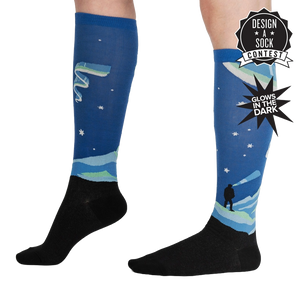 A pair of blue calf-length socks with a black foot and cuff. The socks have an all-over pattern of white and green mountains with a blue sky and white stars.