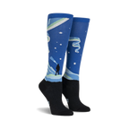 Pair of knee-high socks showcasing a Northern Lights design. Blue, green, and black colors are featured, along with a silhouette of a person watching the lights.