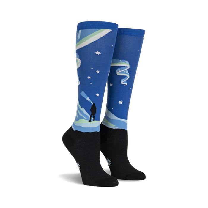 women's blue and black knee-high northern lights glowing socks illuminate the night with stars, mountains, and aurora borealis design.  