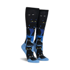 Pair of black and blue knee-high socks with a repeating pattern of black cats. The cats glow in the dark, and the socks have a gradient design.