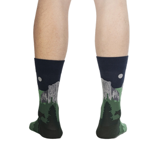 A pair of calf-length socks with a pattern of pine trees and mountains on a dark background.