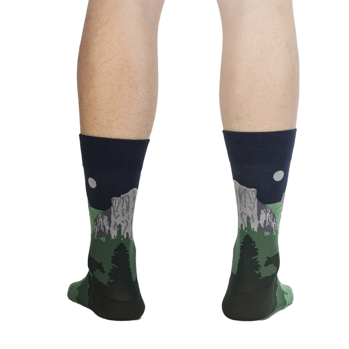 A pair of calf-length socks with a pattern of pine trees and mountains on a dark background.