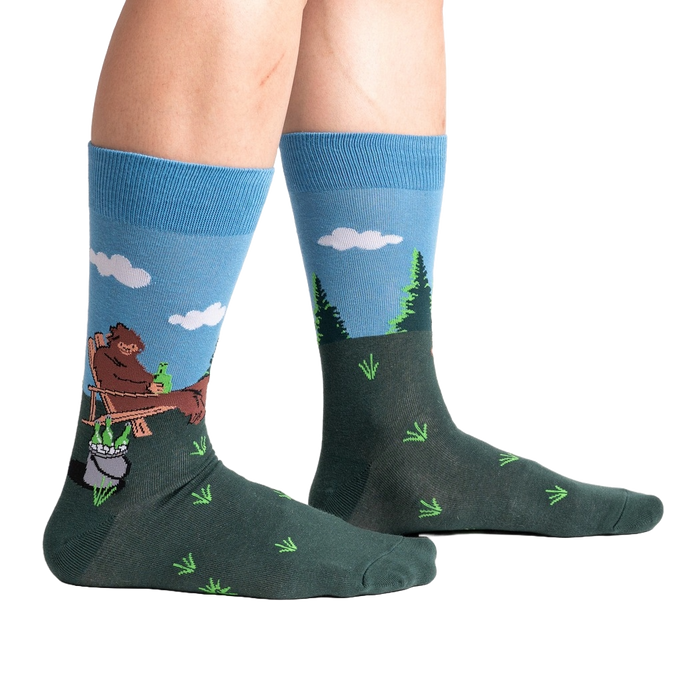 A pair of blue and green socks with a Sasquatch design. The Sasquatch is sitting on a toilet reading a newspaper.