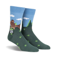 Crew socks in blue and green, depicting a cartoon Bigfoot relaxing in a wooden chair outdoors with a pot and bottles beside him.
