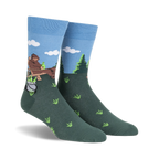 Crew socks in blue and green, depicting a cartoon Bigfoot relaxing in a wooden chair outdoors with a pot and bottles beside him.