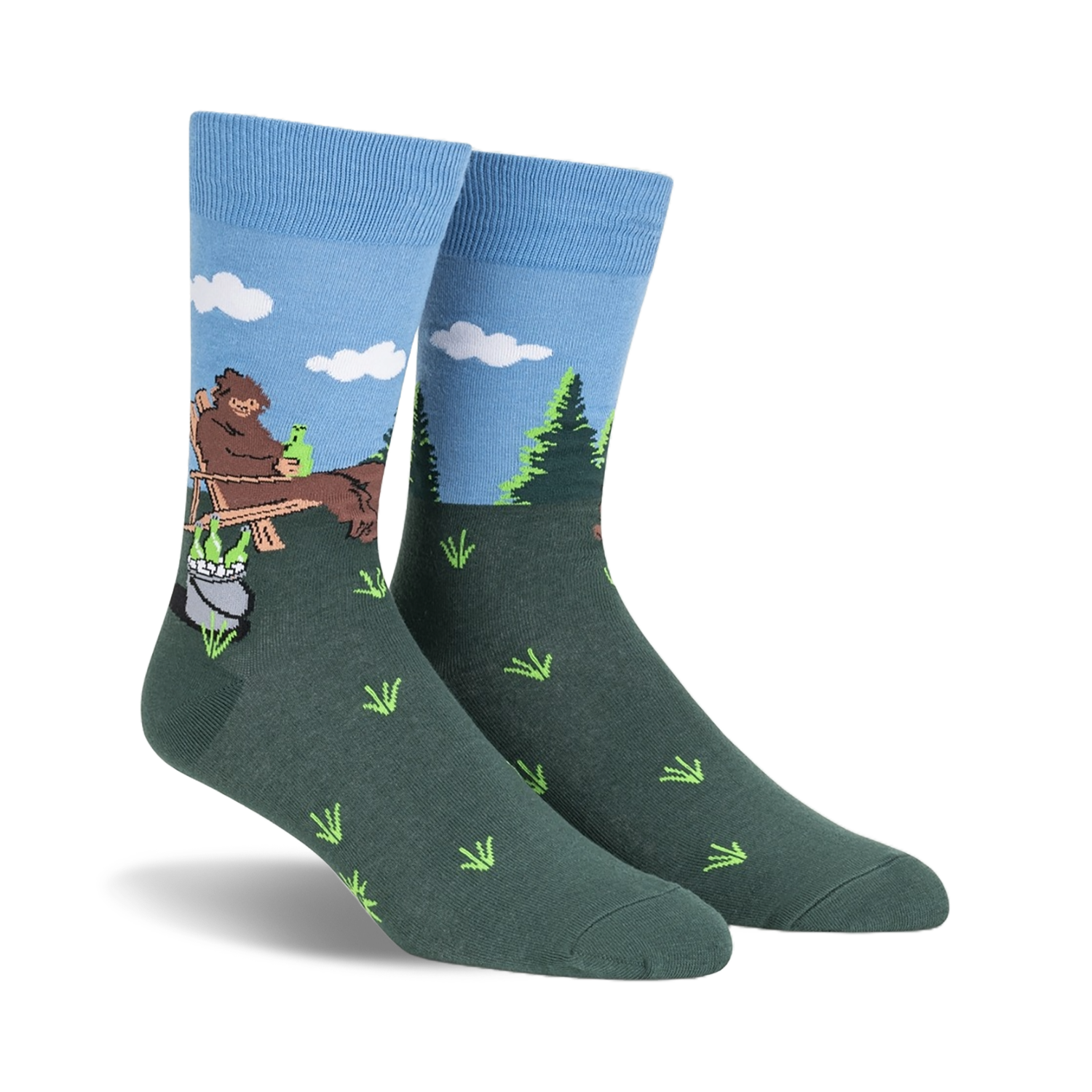 Crew socks in blue and green, depicting a cartoon Bigfoot relaxing in a wooden chair outdoors with a pot and bottles beside him.