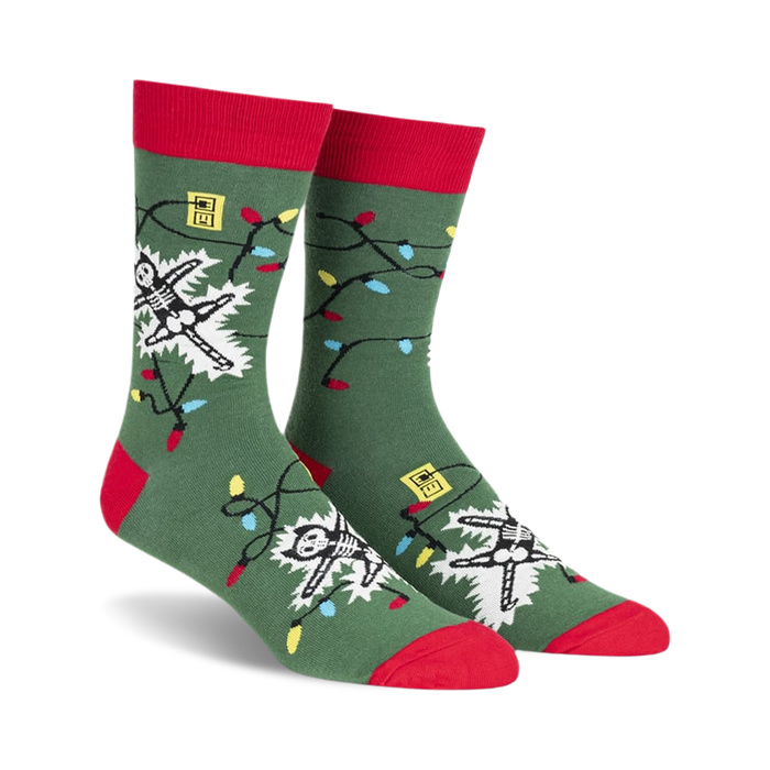 front view of a pair of green socks with red cuffs. the socks feature a white skeleton entangled in christmas lights.  the lights are red, yellow, blue, and green.