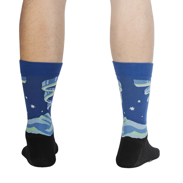 A pair of blue socks with a black heel and toe. The socks have a pattern of white stars and green and blue mountains.