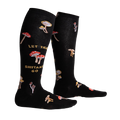 Lifestyle shot showing the 'Let That Shiitake Go' socks on a person's legs. The socks are black with a mushroom and text pattern.