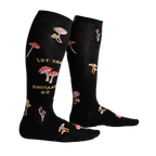 Lifestyle shot showing the 'Let That Shiitake Go' socks on a person's legs. The socks are black with a mushroom and text pattern.