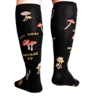 Back view of the 'Let That Shiitake Go' knee-high socks on a person's legs.  The socks show the full design, including the mushroom pattern and text.