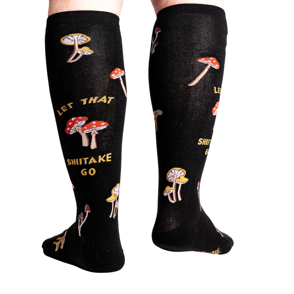 Back view of the 'Let That Shiitake Go' knee-high socks on a person's legs.  The socks show the full design, including the mushroom pattern and text.