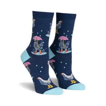 front view of a pair of women's socks with a navy blue background. the socks have a repeating pattern of white chickens with pink umbrellas and yellow rainboots. there are white raindrops scattered across the sock. the socks have a light blue trim at the top.