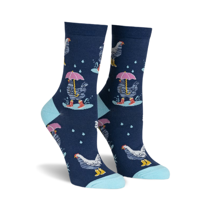 front view of a pair of women's socks with a navy blue background. the socks have a repeating pattern of white chickens with pink umbrellas and yellow rainboots. there are white raindrops scattered across the sock. the socks have a light blue trim at the top.