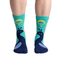 Close-up shot of 'I'm Your Biggest Fan' slipper socks on a person's feet, showcasing the teal and navy peacock design.
