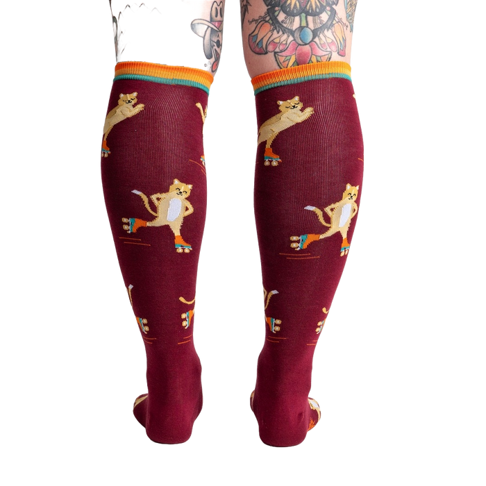 A pair of maroon knee-high socks with a pattern of cartoon cats wearing roller skates.