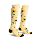 Pair of knee-high socks in pale yellow with a sunflower, bee, and floral design. Black heel and toe.