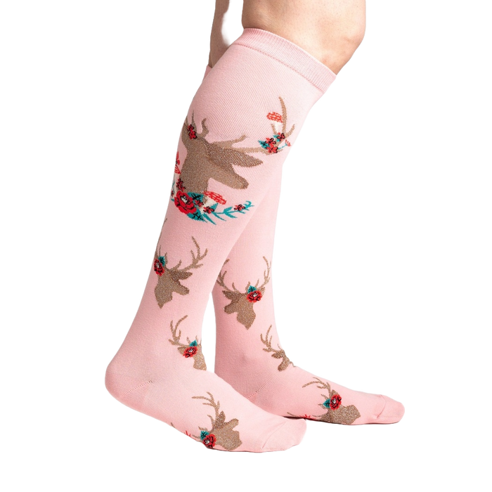 A pair of pink knee-high socks with a pattern of red and green mushrooms, blue and green leaves, and brown deer antlers.
