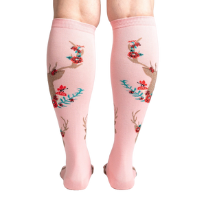 A pair of pink knee-high socks with a pattern of red and green mushrooms, blue and green leaves, and brown deer antlers.