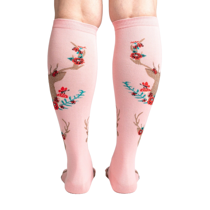 A pair of pink knee-high socks with a pattern of red and green mushrooms, blue and green leaves, and brown deer antlers.