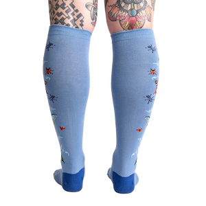 A pair of blue knee-high socks with a pattern of ladybugs, dragonflies, and flowers on them.