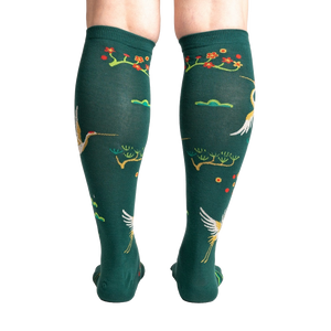 A pair of forest green knee-high socks with a repeating pattern of red-crowned cranes and cherry blossoms on a black background.