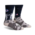 Pair of crew socks; navy blue with astronauts high-fiving on the moon, a US flag, and a lunar landscape. The foot features a grey moon rock pattern.