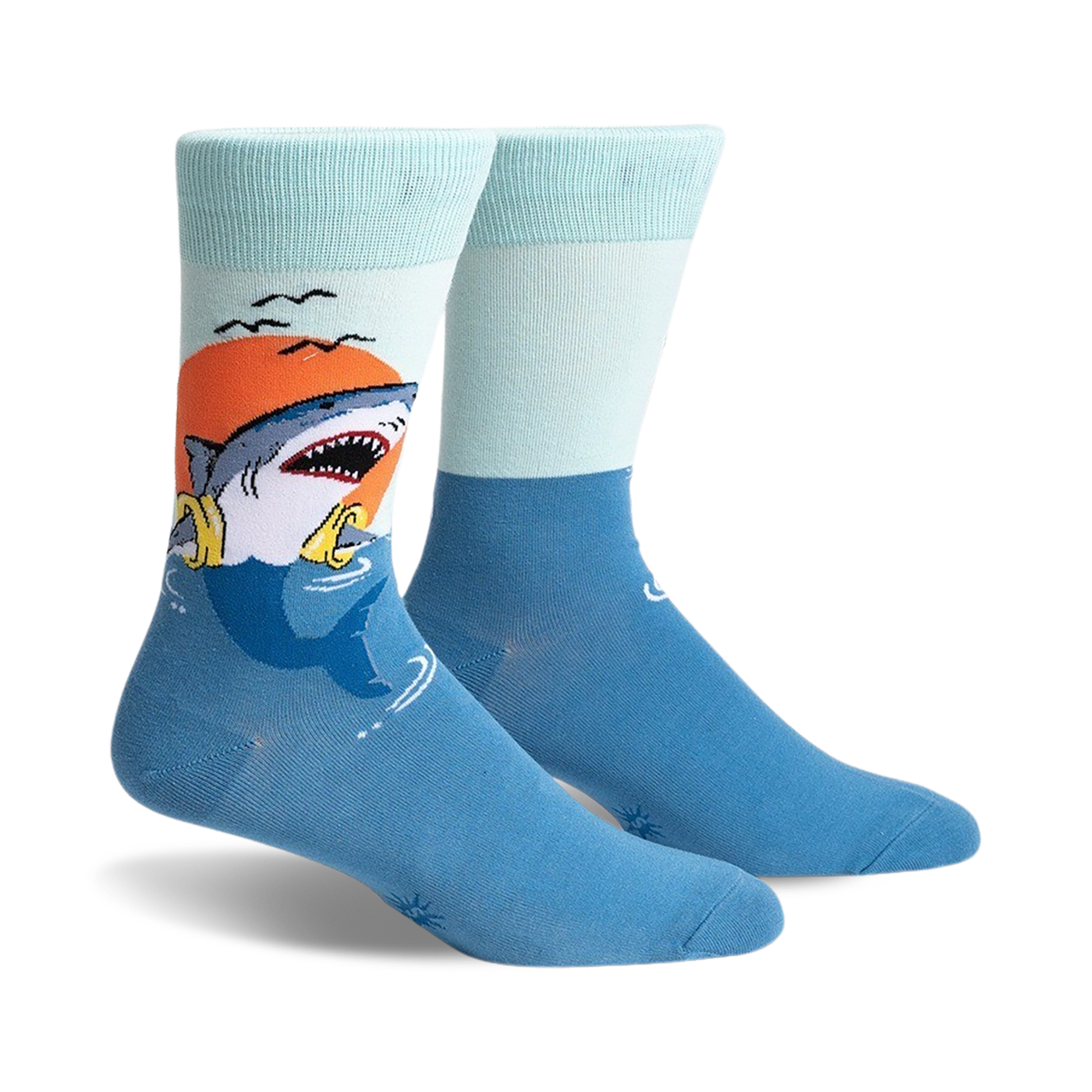 A pair of crew socks with a graphic of a shark catching a life preserver at sunset. The socks are teal and light blue.