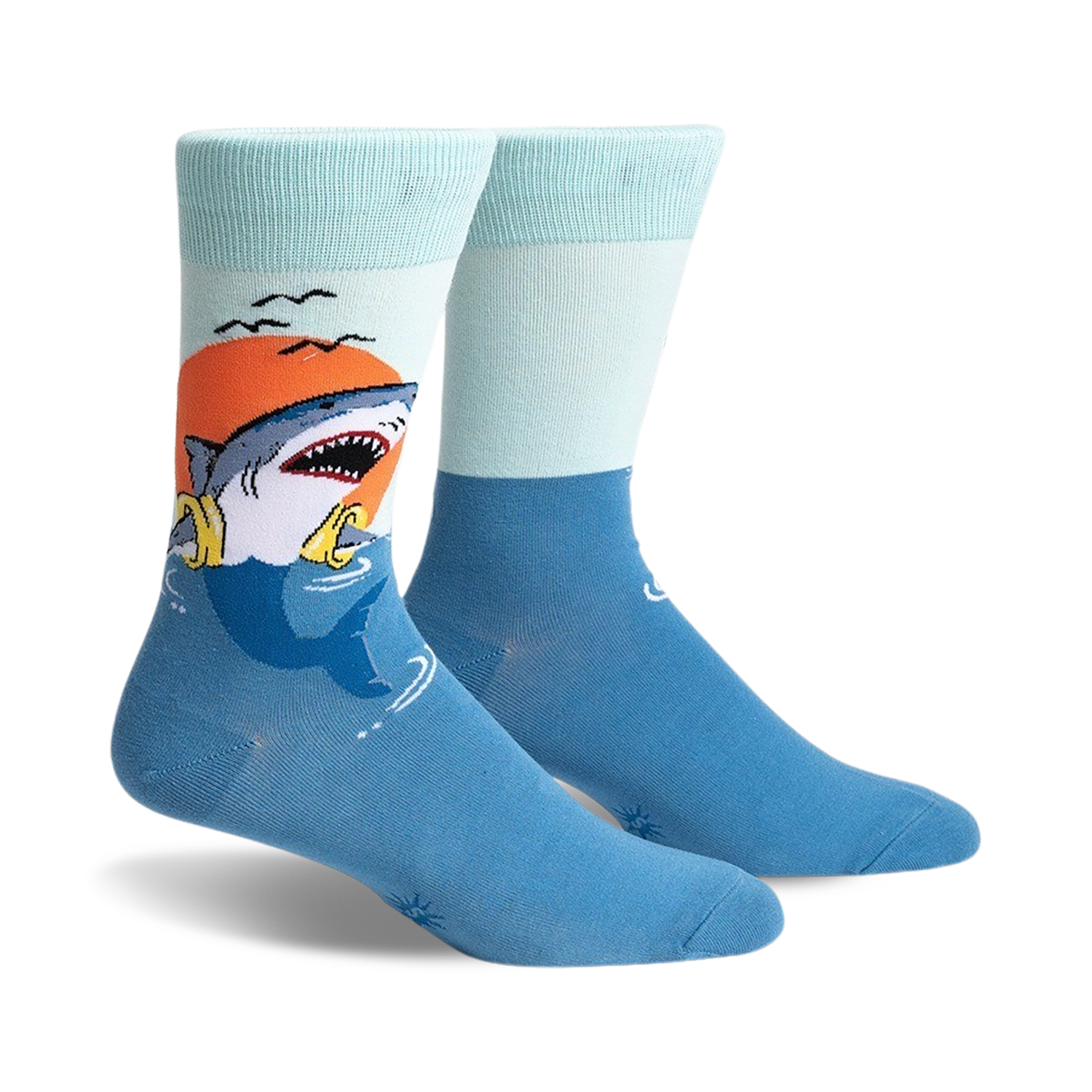 A pair of crew socks with a graphic of a shark catching a life preserver at sunset. The socks are teal and light blue.