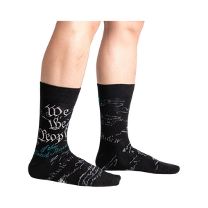 Lifestyle shot showing The Constitution socks on a person's legs. The socks are black with teal and gray text.